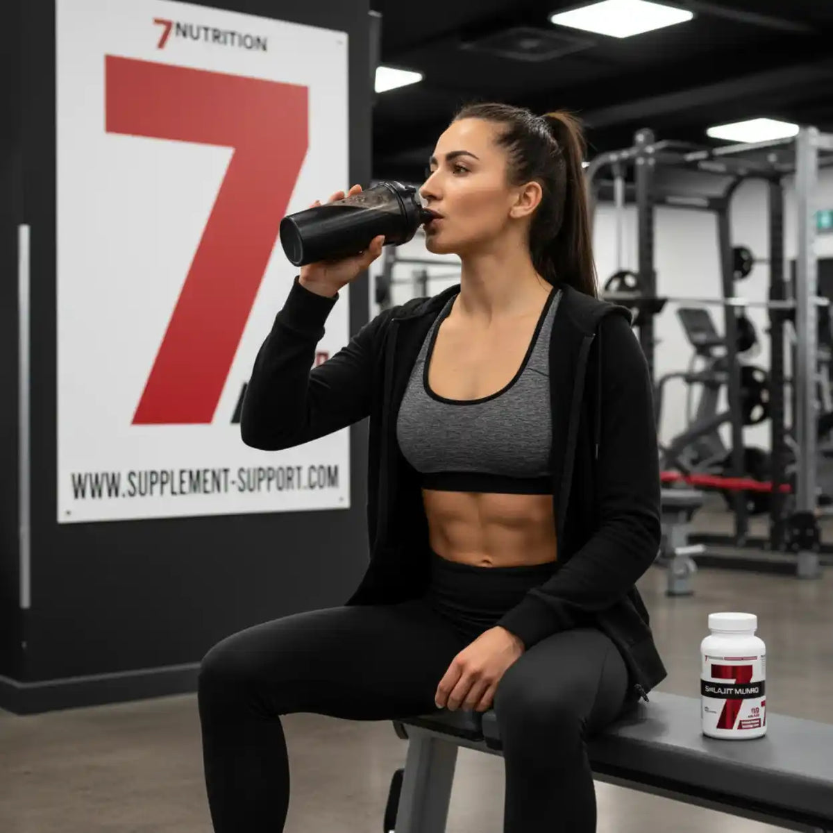 Sportliche Frau trinkt aus schwarzem Shaker im Fitnessstudio