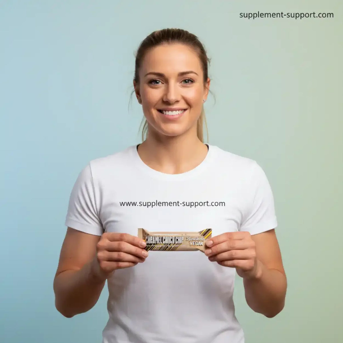Eine Frau in einem weißen T-Shirt hält einen Barebells Vegan Protein Bar in der Geschmacksrichtung Caramel Cookie Chip.