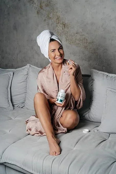 Frau im Bademantel mit Nahrungsergänzungsmittel, entspannt auf Sofa, ideal für Sportler und Fitness