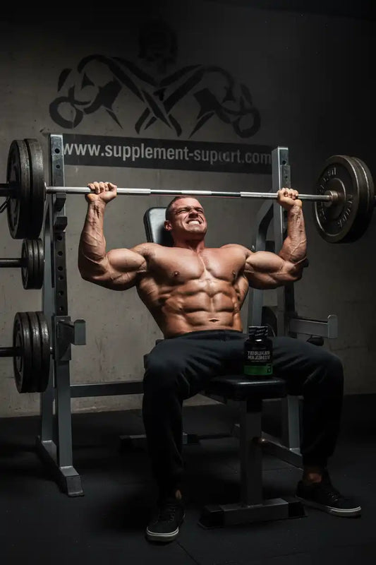 Muskulöser Bodybuilder beim Training mit Langhantel und Nahrungsergänzungsmittel im Fitnessstudio.