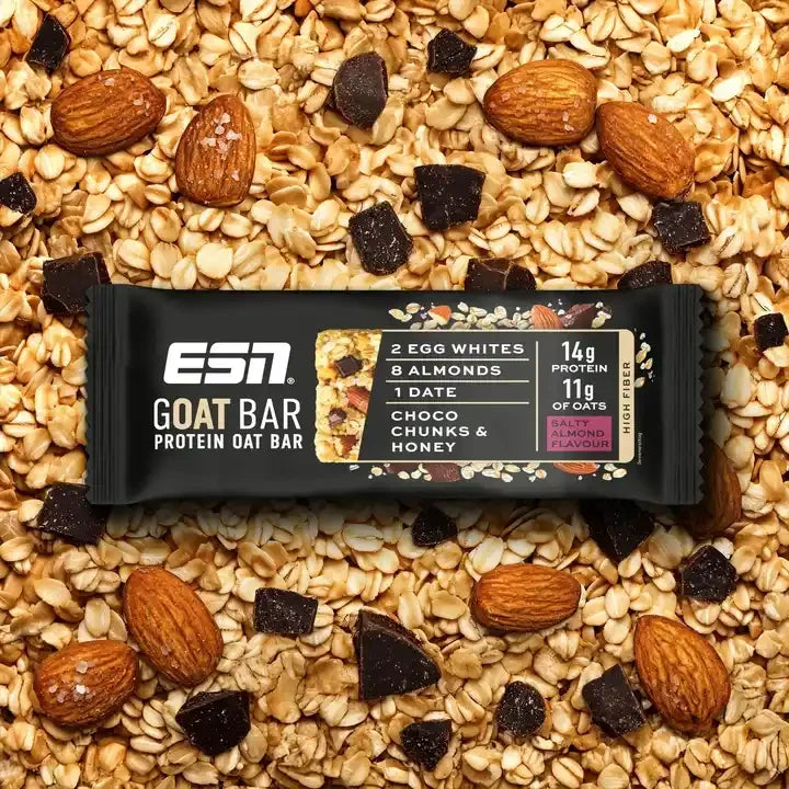 ESN Protein GOAT Oat Bar auf einem Hintergrund aus Haferflocken, Mandeln und Schokoladenstücken.