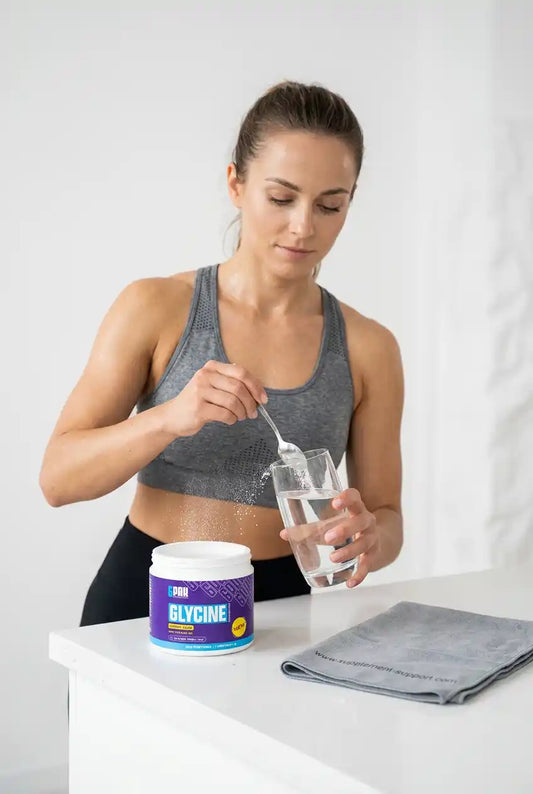 Frau gibt Glycin von TREC NUTRITION mit einem Löffel in ein Glas Wasser.