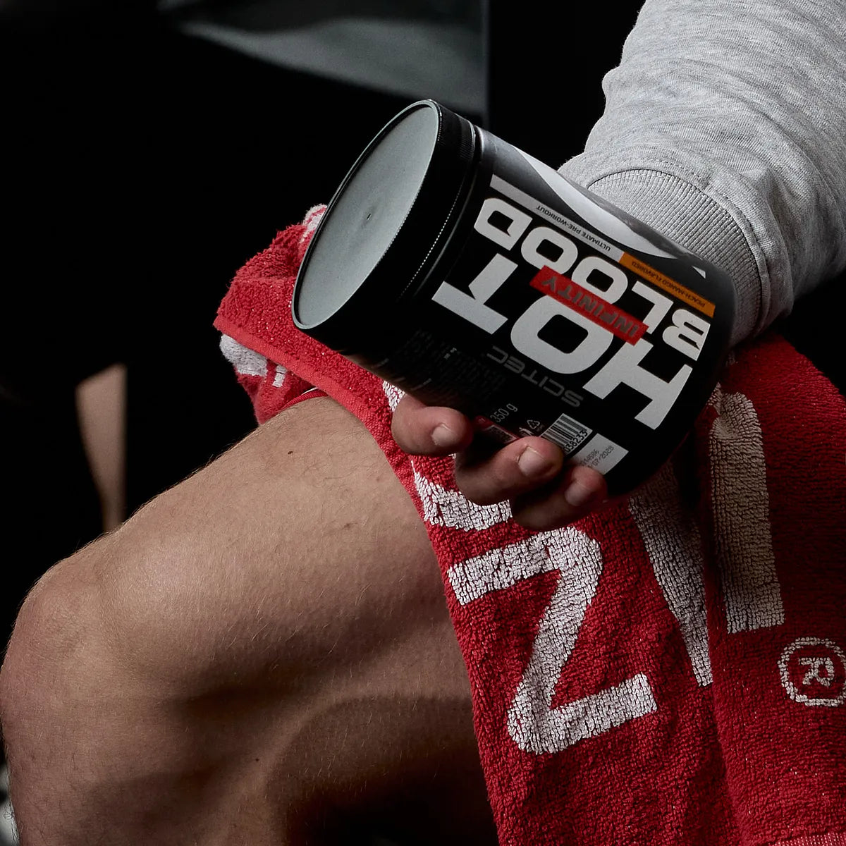 Sportler hält Hot Blood Infinity Booster Dose auf rotem Handtuch, Fokus auf Produktetikett