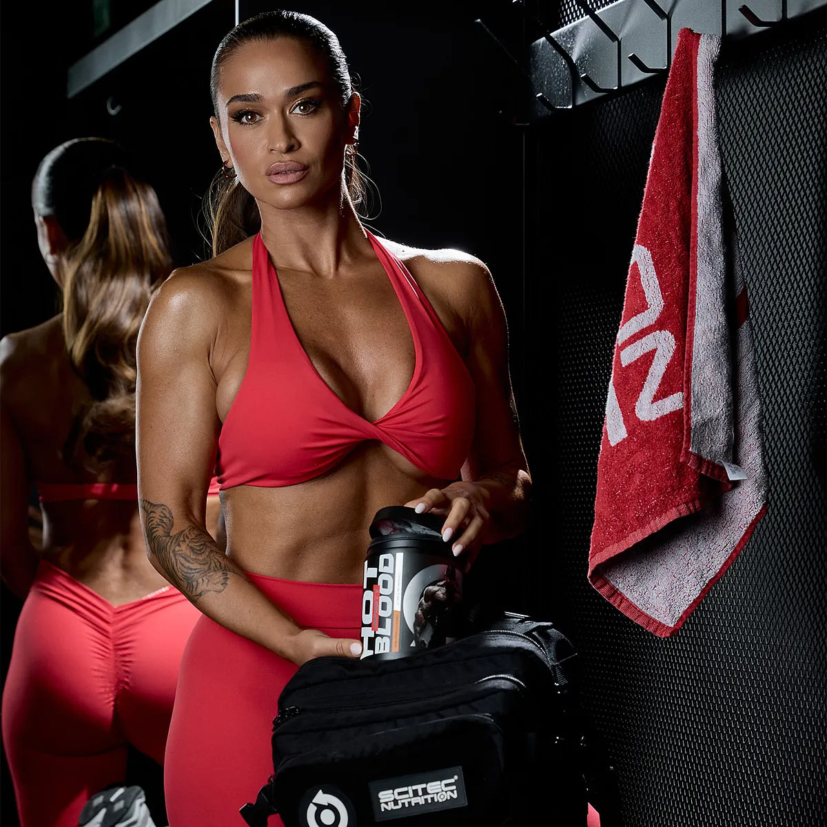 Sportliche Frau im Fitnessstudio mit rotem Outfit, hält Scitec Nutrition Hot Blood Shaker