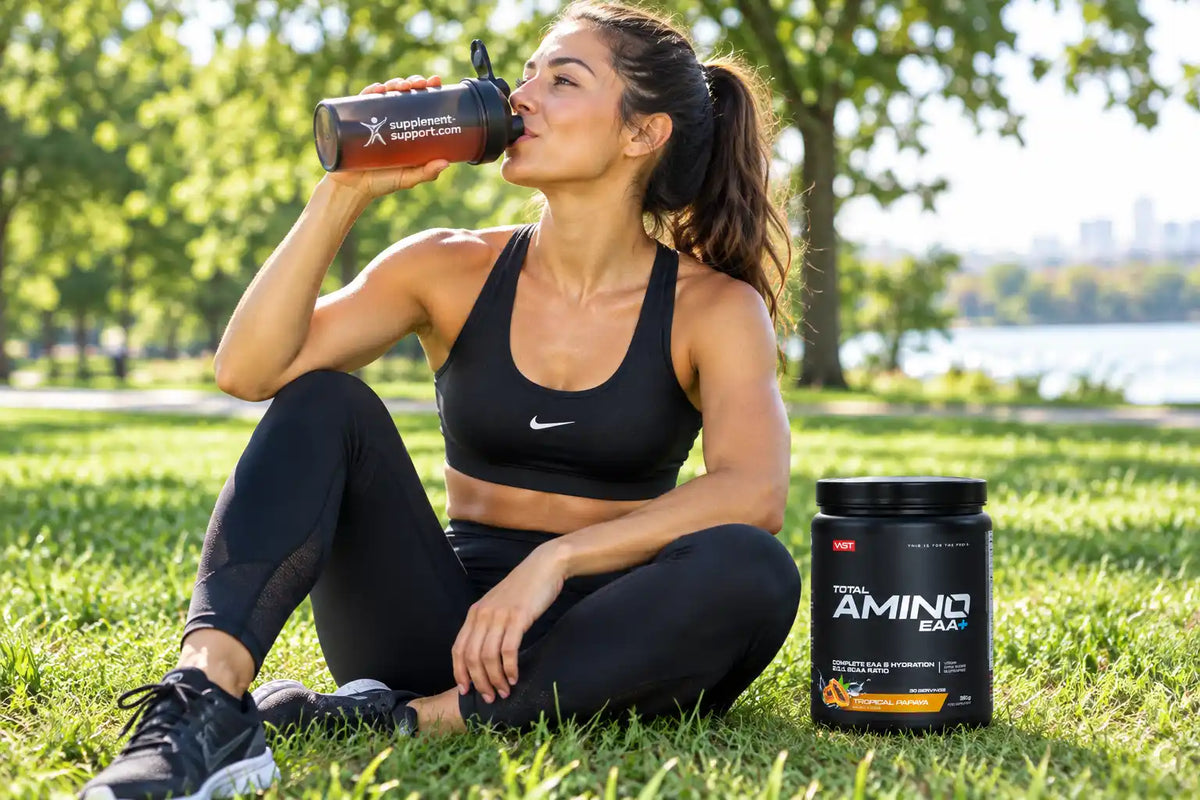 Sportlerin trinkt aus Shaker neben einer Dose VAST® Total Amino EAA+ auf einer grünen Wiese.